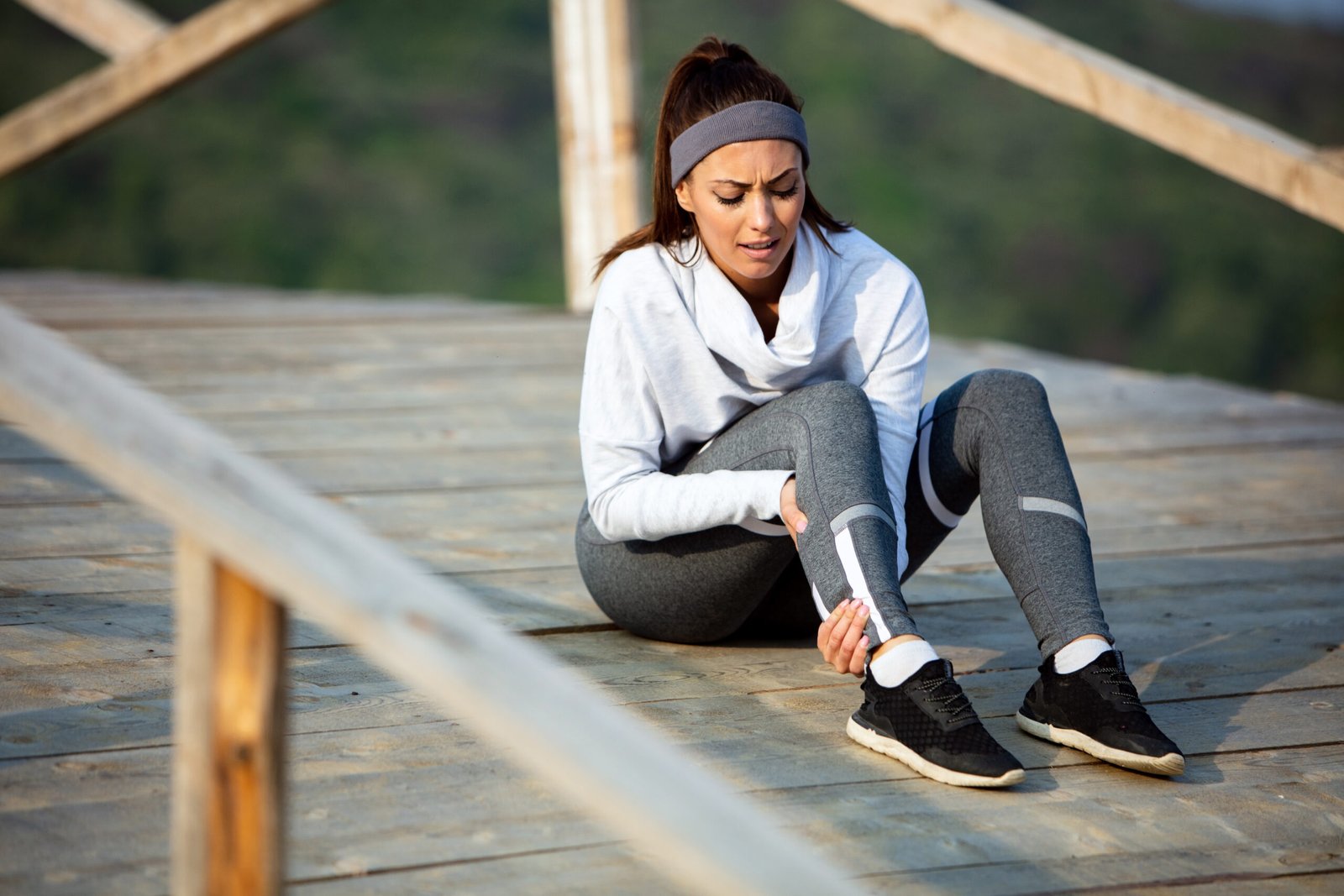 Young athletic woman holding her leg in pain while exercising outdoors